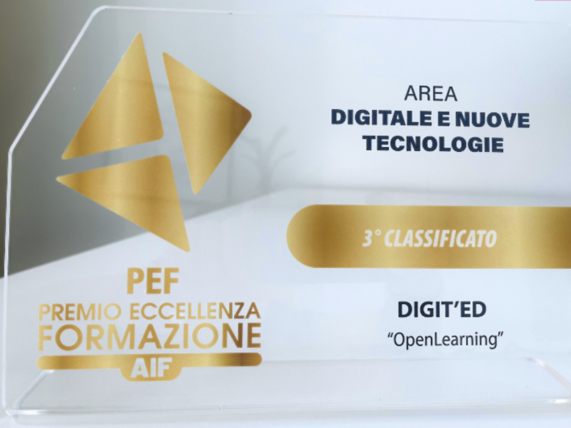 Foto del premio su un tavolo bianco. Premio trasparente con scritte oro "Premio Eccellenza Formazione di AIF" "3° classificato" e scritte blu "area digitale e nuove tecnologie" "Digit'Ed - Open Learning"