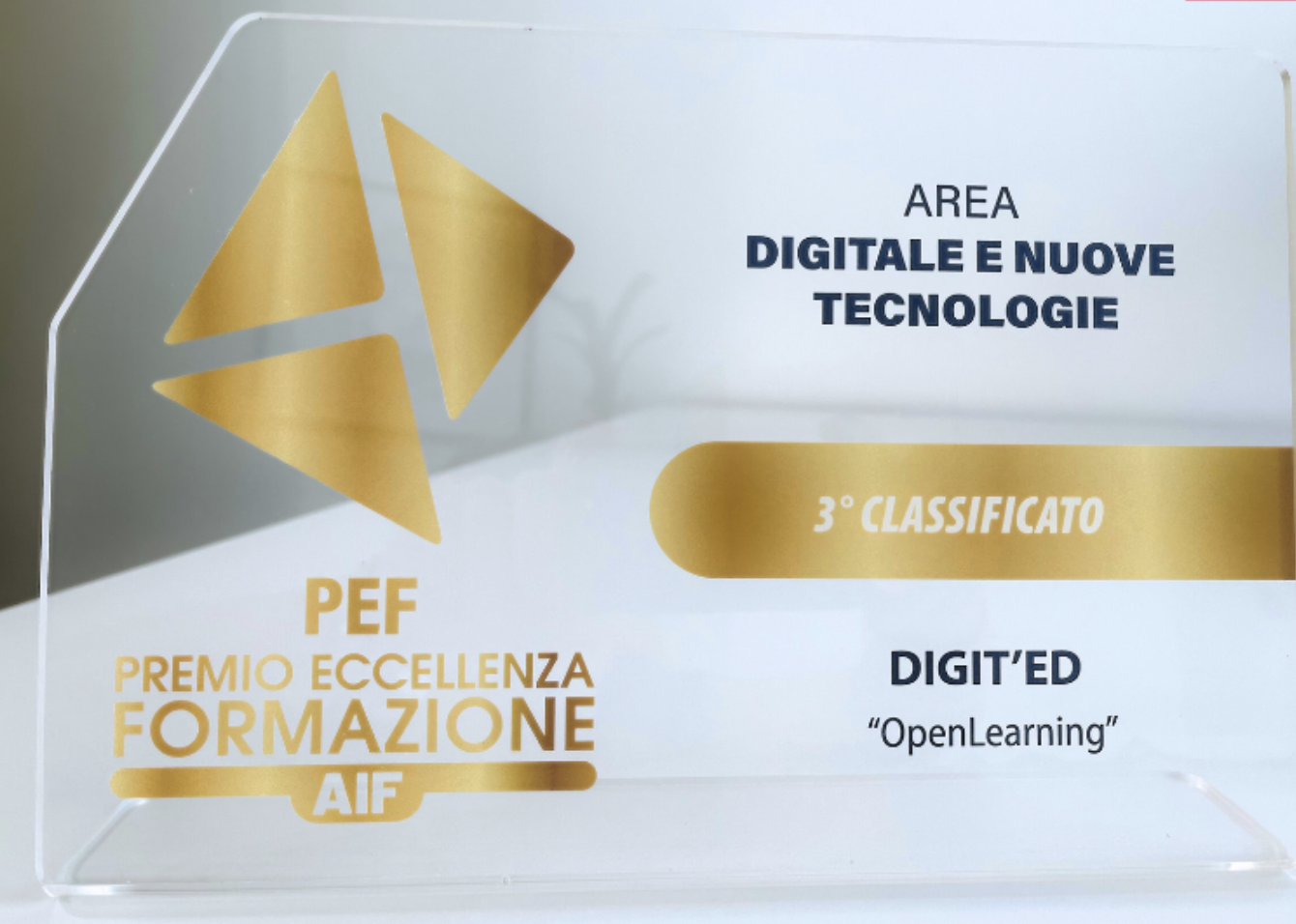 Foto del premio su un tavolo bianco. Premio trasparente con scritte oro "Premio Eccellenza Formazione di AIF" "3° classificato" e scritte blu "area digitale e nuove tecnologie" "Digit'Ed - Open Learning"