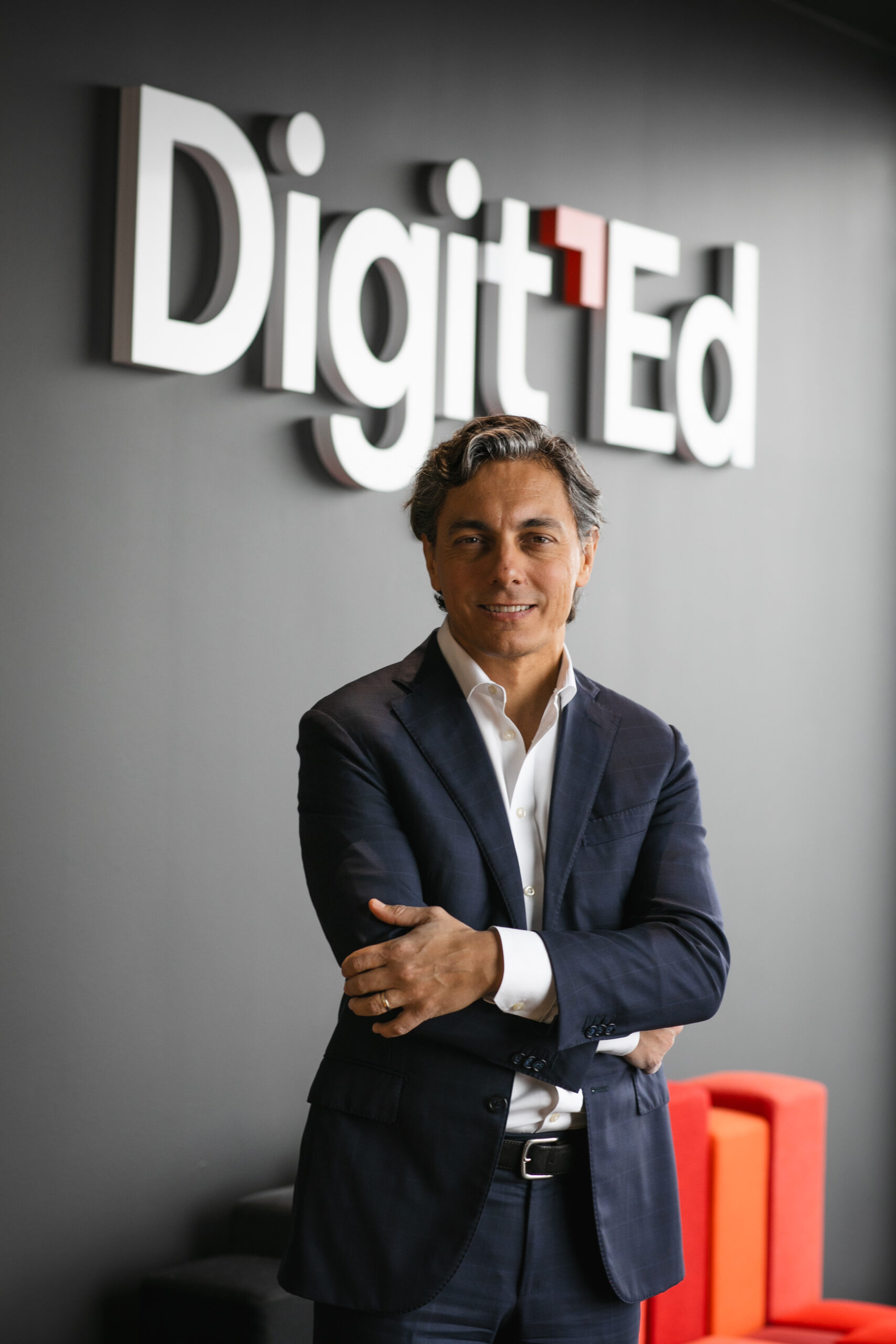 Foto del CEO Davide Vassena in piedi con le braccia in conserte con sfondo del logo Digit'Ed